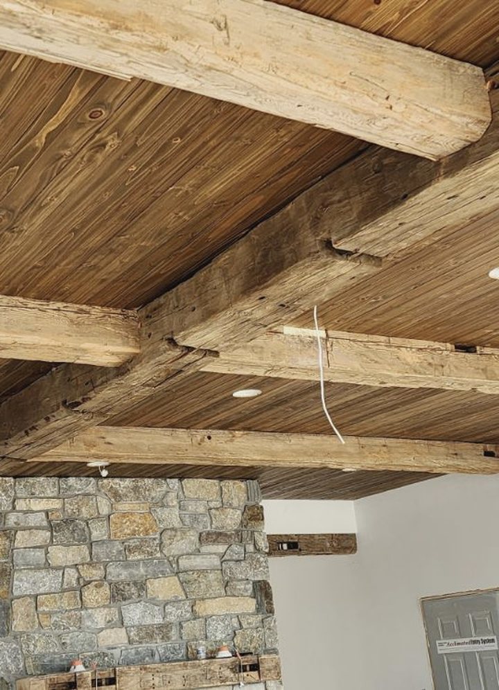 Weathered gray hand hewn mixed hardwood solid beams over a stone fireplace